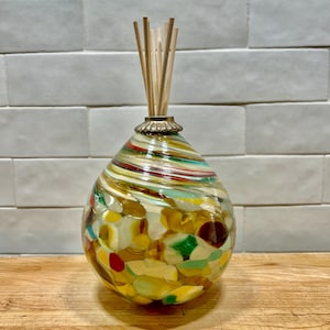 May include: A glass diffuser bottle with a swirl pattern and colorful glass pieces inside. The bottle has a gold metal top and wooden diffuser sticks.