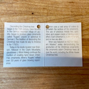 Puede incluir: Una tarjeta blanca con texto sobre adornos navide&ntilde;os, incluyendo la historia del soplado de vidrio y el uso de metales preciosos. La tarjeta menciona al soplador de vidrio J. Wren Helwig y su estudio en Misuri.