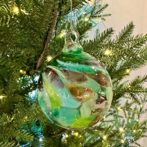 May include: A green, brown, and white glass Christmas ornament with a swirl pattern.