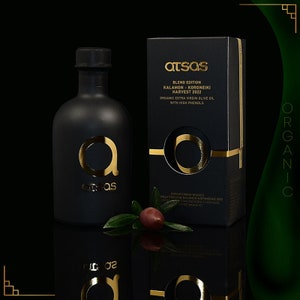 K&ouml;nnte beinhalten: Ein schwarzes Oliven&ouml;lflaschen- und Karton-Set mit goldfarbenen Buchstaben und Akzenten. Die Flasche und die Schachtel tragen den Markennamen "atsas" und den Text "BLEND EDITION KALAMON - KORONEIKI HARVEST 2022 ORGANIC EXTRA VIRGIN OLIVE OIL WITH HIGH PHENOLS". Ein Olivenzweig mit einer Olive befindet sich davor.