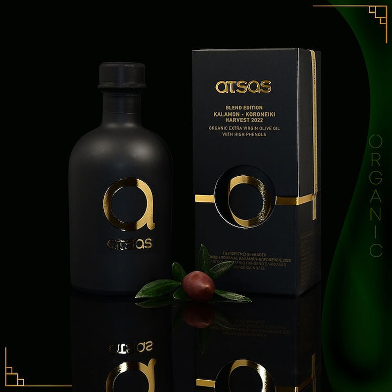 K&ouml;nnte beinhalten: Ein schwarzes Oliven&ouml;lflaschen- und Karton-Set mit goldfarbenen Buchstaben und Akzenten. Die Flasche und die Schachtel tragen den Markennamen "atsas" und den Text "BLEND EDITION KALAMON - KORONEIKI HARVEST 2022 ORGANIC EXTRA VIRGIN OLIVE OIL WITH HIGH PHENOLS". Ein Olivenzweig mit einer Olive befindet sich davor.