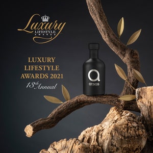 Puede incluir: Una botella de vidrio negro con una etiqueta plateada que dice "atsas" y una gran letra plateada "a" en la parte delantera. La botella est&aacute; sentada en una rama de un &aacute;rbol con hojas doradas. El texto "Luxury Lifestyle Awards 2021 13th Annual" est&aacute; en el fondo.