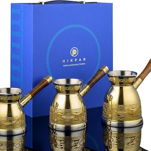May include: A set of three gold-colored Turkish coffee pots with wooden handles. The pots have a decorative pattern and are displayed in front of a blue box with the text "NIKPAR Greek Luxuriousness Creation".