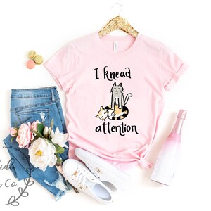 May include: Pink t-shirt with a graphic of two cats and the text "I knead attention".
