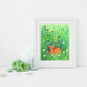 K&ouml;nnte beinhalten: Ein gerahmter Kunstdruck mit einer orangefarbenen Katze mit herzf&ouml;rmiger Brille, die in einem Feld aus gr&uuml;nem Gras, Blumen und Bl&auml;ttern liegt. Das Kunstwerk befindet sich in einem wei&szlig;en Rahmen mit wei&szlig;em Hintergrund. Eine Kerze, eine Glasflasche und gr&uuml;ne Rosen befinden sich im Vordergrund.