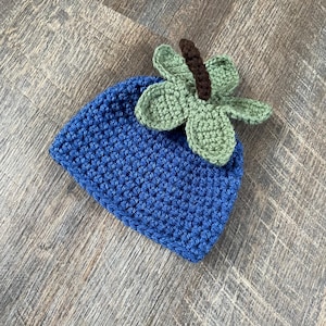 May include: A blue crocheted hat with a green crocheted butterfly on top.