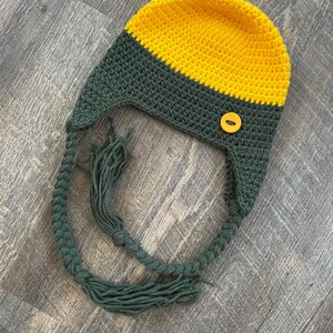 May include: A green and yellow crocheted hat with a button and long green tassels.