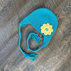 May include: A turquoise crocheted hat with a yellow flower and a turquoise tassel.