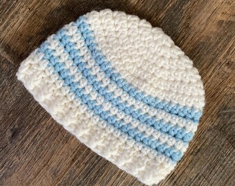 May include: A white crocheted beanie with blue stripes. The beanie is made with a soft yarn and has a simple design.
