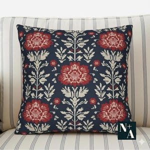 May include: Square cushion featuring a navy blue backdrop with a repeating floral design in red and off-white. The cushion is placed on a striped upholstered surface.