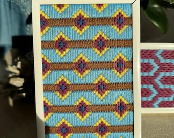 May include: A framed piece of needlepoint with a geometric pattern in shades of blue, brown, yellow, and red.
