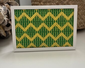 May include: A framed green and yellow geometric pattern needlepoint design. The needlepoint is in a white frame.