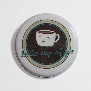 May include: A white button with a brown coffee cup with a smiling face and the text "little cup of joe" in teal blue lettering.