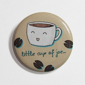 May include: A beige button with a cartoon coffee cup with a smiling face and the text "little cup of joe..." printed on it. The button is surrounded by brown coffee beans.