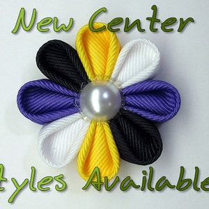 May include: A purple, black, white, and yellow flower made of ribbon with a pearl in the center. The text "New Center Styles Available!" is written below the flower.
