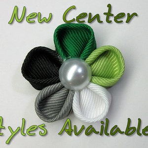 May include: A five-petal flower hair clip made of green, black, gray, and white ribbon. The center of the flower has a pearl-like bead. The text "New Center Styles Available!" is written in green letters on a white background.