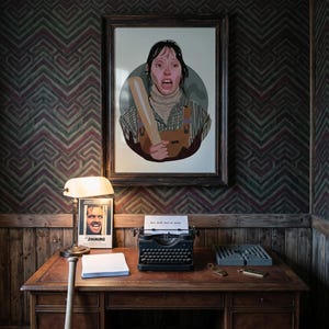 May include: A framed print of a person holding a baseball bat, with a distressed expression. A vintage typewriter sits on a wooden desk, with a sheet of paper that reads "All work and no play". A lamp and a poster are also on the desk.