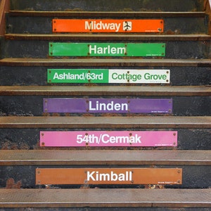 May include: A set of six signs with the names of Chicago 'L' train stations: Midway, Harlem, Ashland/63rd, Cottage Grove, Linden, 54th/Cermak, and Kimball. The signs are attached to the steps of a staircase.
