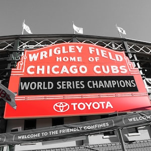 May include: A red and white sign with the text "Wrigley Field, Home of Chicago Cubs, World Series Champions" and a Toyota logo. The sign is attached to a black metal structure.