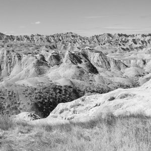 May include: A black and white photograph of a vast, rugged landscape with rolling hills and valleys. The landscape is covered in dry, brushy vegetation.