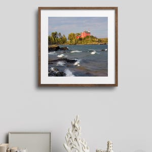 May include: A framed photograph of a red lighthouse on a rocky island with choppy water in the foreground.