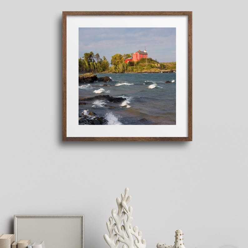 May include: A framed photograph of a red lighthouse on a rocky island with choppy water in the foreground.