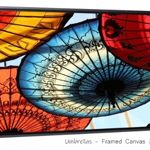 May include: A framed canvas print of colorful umbrellas with intricate designs. The umbrellas are arranged in a circular pattern, with the blue umbrella in the center. The print is 24 inches by 36 inches.
