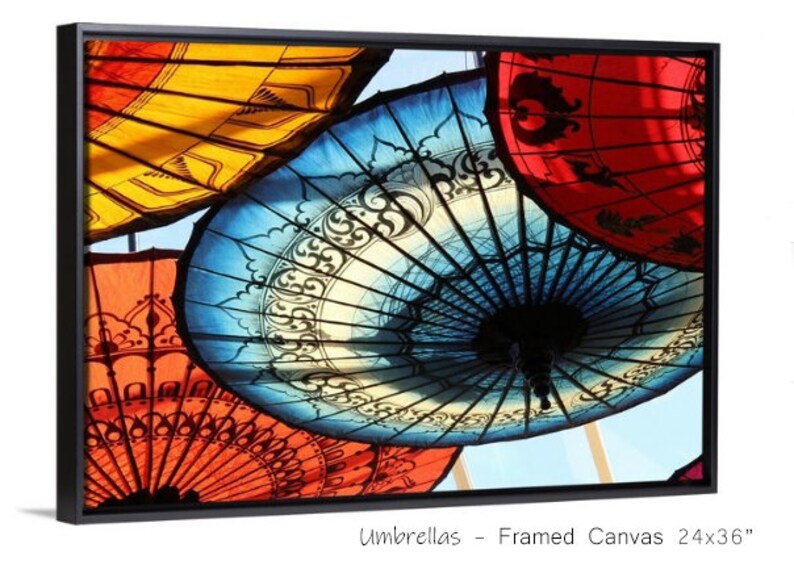 May include: A framed canvas print of colorful umbrellas with intricate designs. The umbrellas are arranged in a circular pattern, with the blue umbrella in the center. The print is 24 inches by 36 inches.