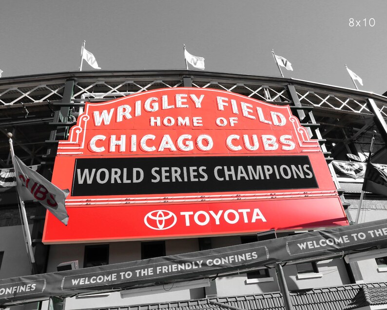 May include: A red and white sign with the words "Wrigley Field, Home of Chicago Cubs, World Series Champions" and the Toyota logo. The sign is attached to a building with a black and white checkered pattern.