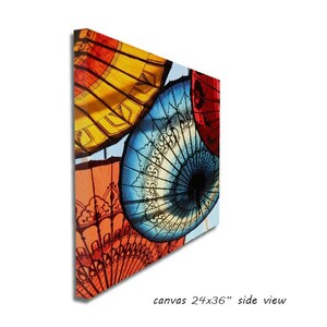 May include: A colorful canvas print featuring a close-up of several traditional umbrellas with intricate designs. The umbrellas are red, yellow, blue, and white. The canvas is 24 inches by 36 inches.