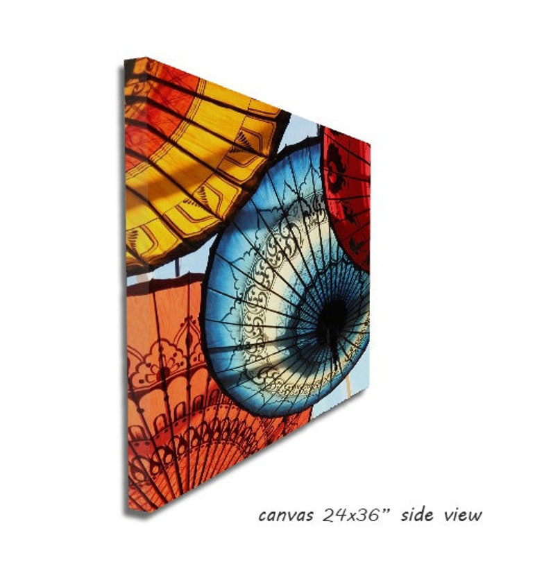 May include: A colorful canvas print featuring a close-up of several traditional umbrellas with intricate designs. The umbrellas are red, yellow, blue, and white. The canvas is 24 inches by 36 inches.