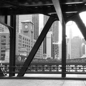 Puede incluir: Una fotograf&iacute;a en blanco y negro de un puente con vista al horizonte de la ciudad. El puente est&aacute; hecho de acero y tiene un patr&oacute;n de cuadr&iacute;cula. El horizonte de la ciudad est&aacute; en el fondo e incluye edificios altos.