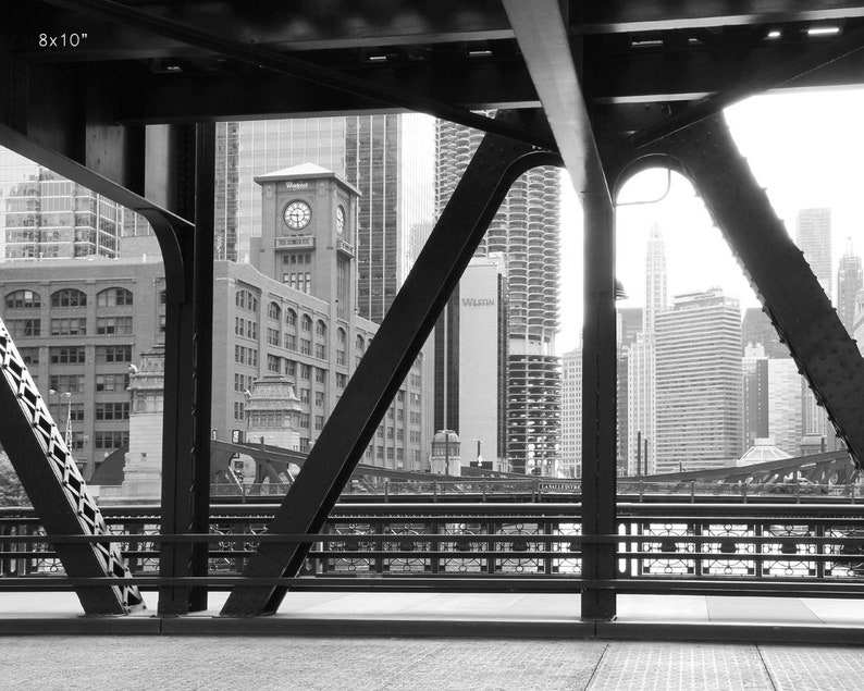 Puede incluir: Una fotograf&iacute;a en blanco y negro de un puente con vista al horizonte de la ciudad. El puente est&aacute; hecho de acero y tiene un patr&oacute;n de cuadr&iacute;cula. El horizonte de la ciudad est&aacute; en el fondo e incluye edificios altos.