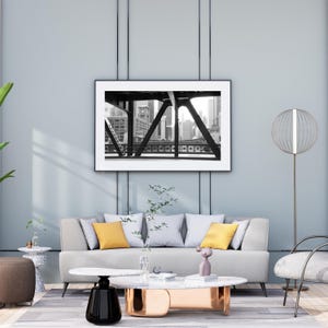 Puede incluir: Un sof&aacute; blanco con almohadas amarillas se encuentra en una sala de estar con una foto en blanco y negro de un puente sobre una ciudad. Una mesa de caf&eacute; blanca con una base negra y dorada se encuentra frente al sof&aacute;. Una peque&ntilde;a escultura abstracta rosa se encuentra sobre la mesa de caf&eacute;.