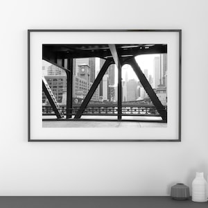 Puede incluir: Fotograf&iacute;a en blanco y negro de un horizonte urbano visto a trav&eacute;s de las vigas de acero de un puente.