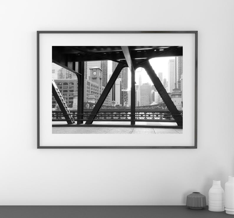 Puede incluir: Fotograf&iacute;a en blanco y negro de un horizonte urbano visto a trav&eacute;s de las vigas de acero de un puente.
