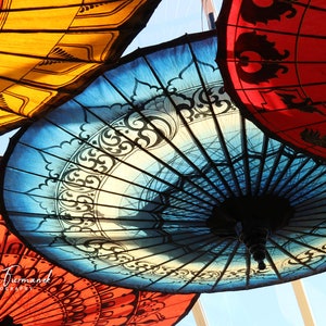 May include: A collection of colorful, patterned umbrellas hanging from the ceiling. The umbrellas are made of fabric and have intricate designs. The umbrellas are a variety of colors, including red, blue, yellow, and white.