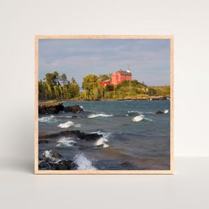 May include: A red lighthouse sits on a rocky island with a view of the blue water and white waves crashing on the shore.