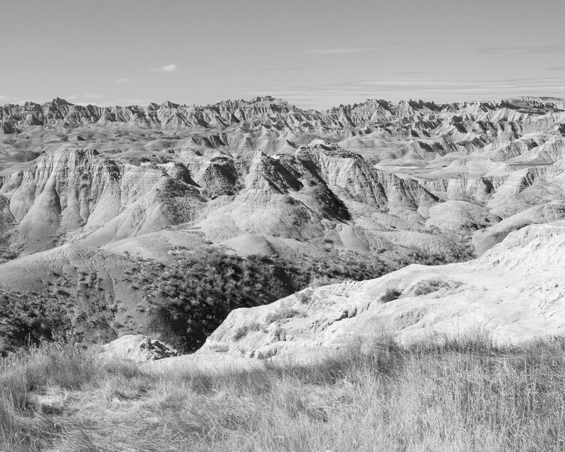 May include: A black and white photograph of a vast, rugged landscape with rolling hills and valleys. The landscape is covered in dry, brown grass and appears to be a desert or semi-desert environment.