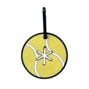 May include: A circular luggage tag with a tennis ball design. The tag is yellow with white curved lines and a black border. A black clip is attached at the top, and a white asterisk shape is in the centre.