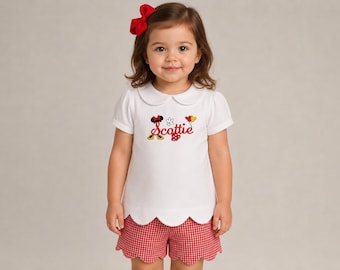 May include: A white short-sleeved shirt with a rounded collar and scalloped hem, featuring the embroidered name Scottie in red script, surrounded by small cartoon mouse-themed icons. Paired with red and white gingham shorts with a scalloped hem.