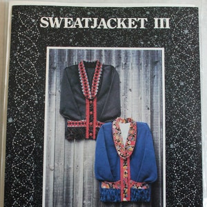 May include: A sewing pattern for a sweatjacket, titled "Sweatjacket III" from "A Quilter's Wardrobe". The pattern shows two different versions of the jacket, one in black and one in blue, both with colorful patchwork details.