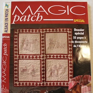 May include: A magazine cover featuring a red and white patchwork quilt with embroidered scenes of people and buildings. The magazine is titled "Magic Patch" and has a special edition focused on Alsace, France. The text "l'Alsace en patch" is also featured on the cover.
