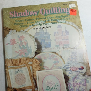 May include: A book titled "Shadow Quilting" with a pink and white cover featuring a variety of quilted projects. The book features 9 projects and includes full-size patterns and a stitch guide.