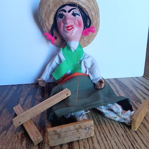May include: A traditional Mexican puppet with a straw hat, green and orange clothing, and wooden control sticks. The puppet is made of fabric and has a painted face.