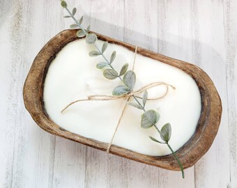 May include: A white candle in a wooden dough bowl with a sprig of greenery tied with twine.