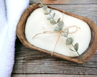 May include: A white candle in a wooden bowl with a sprig of greenery tied with twine. The candle is in the shape of a loaf of bread.