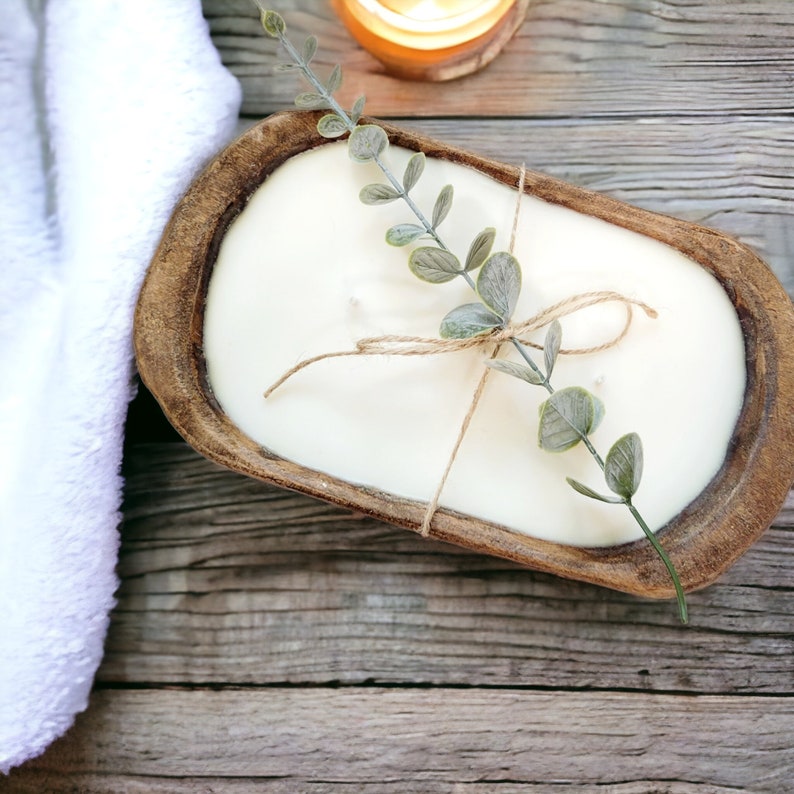 May include: A white candle in a wooden bowl with a sprig of greenery tied with twine. The candle is in the shape of a loaf of bread.