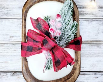 May include: A wooden dough bowl with a white base and a red and black plaid ribbon tied around it. The bowl is decorated with a sprig of frosted pine and red berries.
