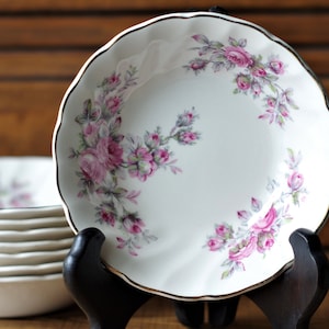 May include: A set of white ceramic bowls with a pink and grey floral design. The bowls have a scalloped edge and a gold rim.